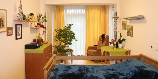 Ein mit Pflegebett, Sitzecke und Kommoden ausgestattetes Bewohnerzimmer.