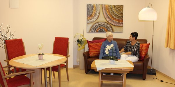Eine Pflegerin unterhält sich mit einer älteren Dame in der gemütlichen Sitzecke.