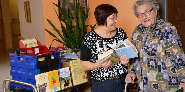 Eine Pflegerin zeigt einer Bewohnerin neue Bücher in der mobilen Bücherei.