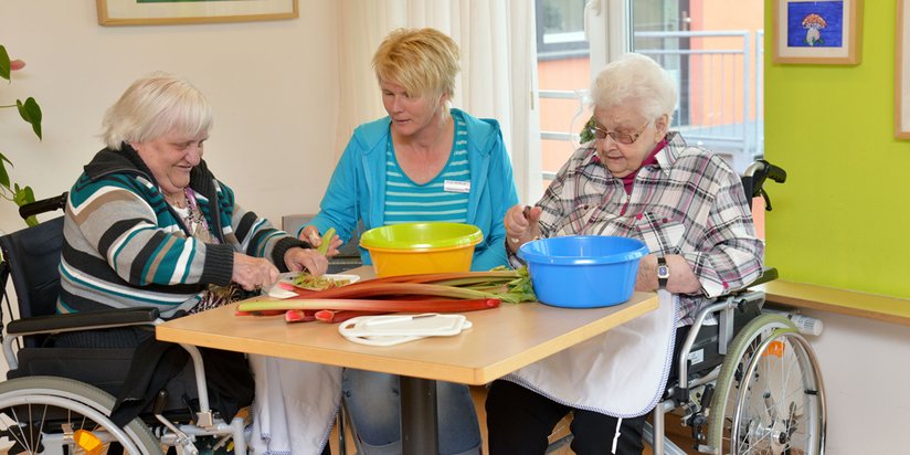 Eine ehrenamtliche Mitarbeiterin schneidet gemeinsam mit zwei Seniorinnen Gemüse.